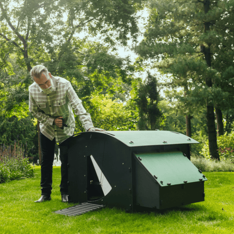 Nestera kunststof kippenhok groot sfeerfoto schuin zijaanzicht, op het gras in een achtertuin met een man die het kippenluik opent.