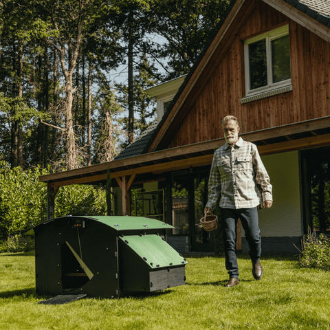 Nestera kunststof kippenhok groot sfeerfoto vooraanzicht, op het gras in een achtertuin met een man die met een mand in zijn hand van een huis naar het kippenhok loopt.