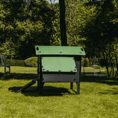 Sfeerfoto Nestera kunststof kippenhok op poten, schuin zijaanzicht op het gras in een achtertuin.