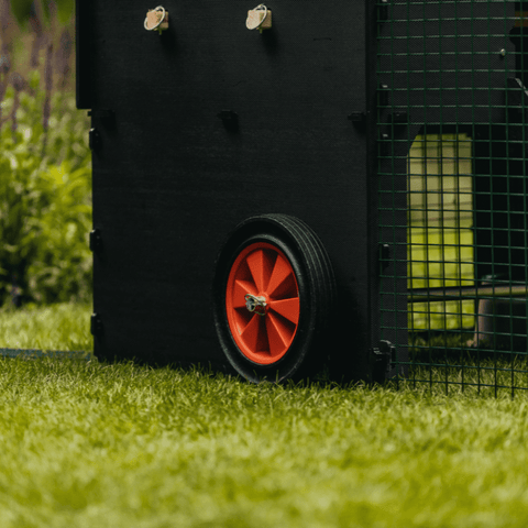 Sfeerfoto Nestera kunststof kippenhok groot op poten, schuin zijaanzicht en ingezoomd op de wielen. Aan de rechterkant zit de ren bevestigd aan het kippenhok.